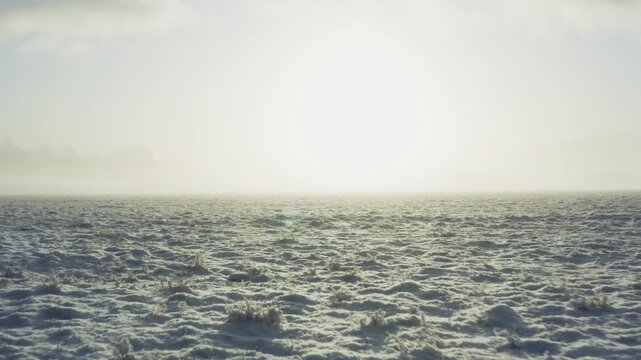 Snow-covered Icelandic plain glows in bright sunlight as drone climbs quickly.