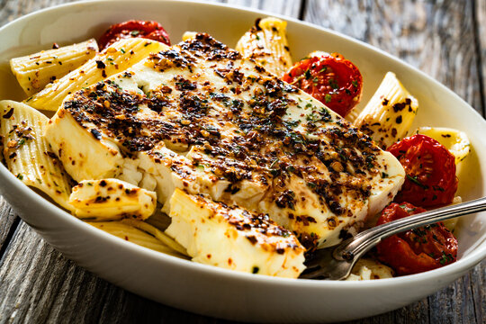 Penne pasta with roasted cherry tomatoes and feta cheese in bowl on wooden table.
