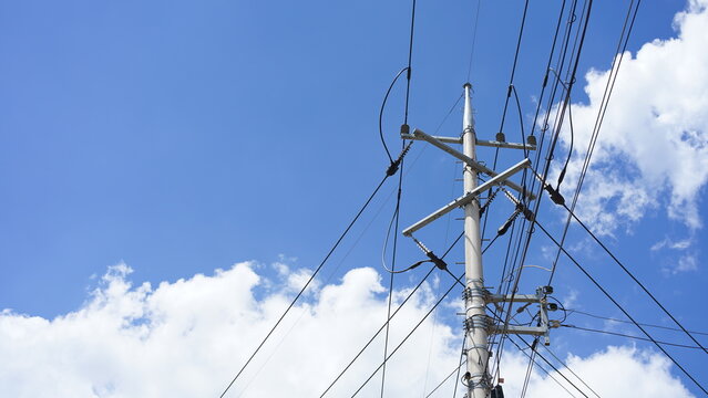 A towering utility pole with neatly aligned power lines rising against a breathtaking blue sky, where soft white clouds create a clean, vibrant, and visually striking backdrop.