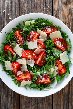 Arugula salad with tomatoes and parmesan cheese on wooden table
