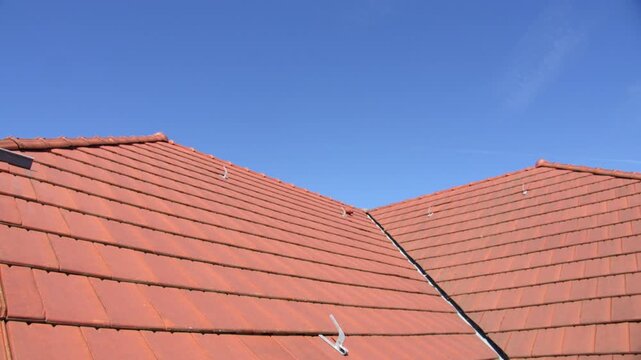 Red residential rooftop with clay tiles moving under a clear blue sky in bright sunlight