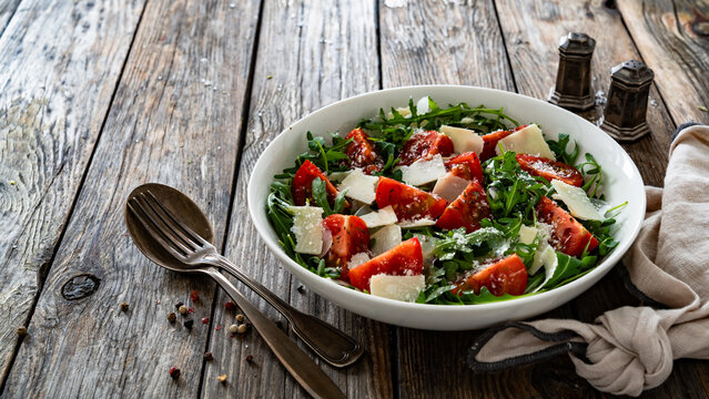 Arugula salad with tomatoes and parmesan cheese on wooden table
