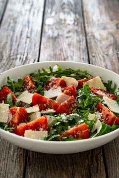 Arugula salad with tomatoes and parmesan cheese on wooden table
