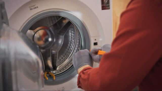 A professional worker disassembles a washing machine with a special tool in the bathroom. The process of disassembling the washing machine drum and removing the rubber cover