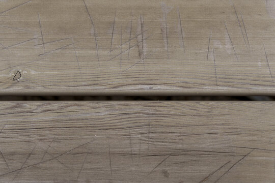 Scratched surface of weathered grey wooden planks with prominent natural grain texture. Rustic background pattern featuring deep cuts and age lines on timber decking.