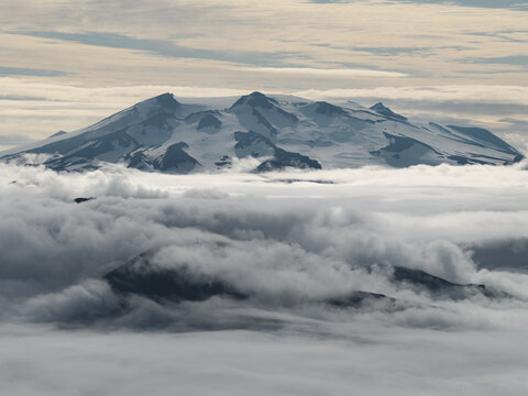 Aerial view of the snow-capped Makushin Volcano rising above a thick layer of clouds in the Aleutian Islands, Unalaska, Alaska, United States.