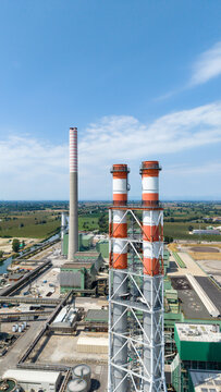 Aerial view of the Tavazzano-Montanaso thermal power plant with tall striped chimneys and industrial structures set amidst green fields in Tavazzano con Villavesco, Lombardy, Italy.