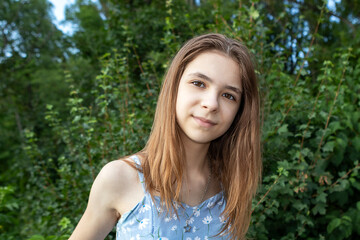 Naklejka premium Outdoor portrait of a teen girl with long hair smiling gently in a green summer setting
