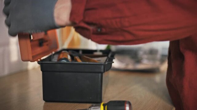 A technician in work clothes and gloves prepares to perform a home repair. He places tools in a special work box. The concept of a home repairman. A work box with tools
