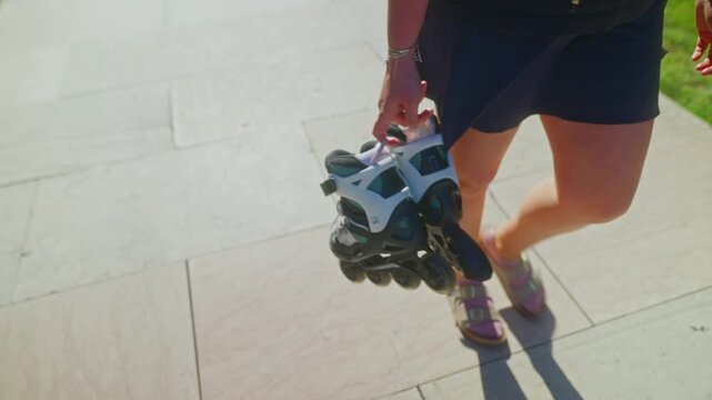 A Person Walking with Rollerblades: Enjoying a Sunny Day Outdoors While Carrying Inline Skates in a Leisurely Stroll by a Paved Pathway