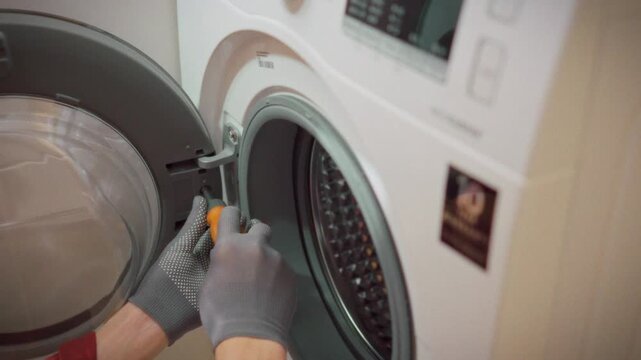 A technician wearing gloves disassembles a washing machine drum, removing a screw in a bathroom. Concept for professional home appliance service and repair