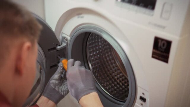 Close-up of gloved hands removing a screw from a washing machine drum in a bathroom. Concept for DIY home appliance repair and saving on technician services