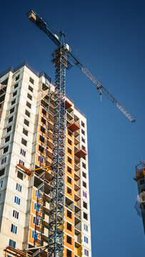 Modern residential tower rises beneath clear blue sky while tower crane supports ongoing construction. Apartment development reflects urban growth, engineering precision and real estate investment.