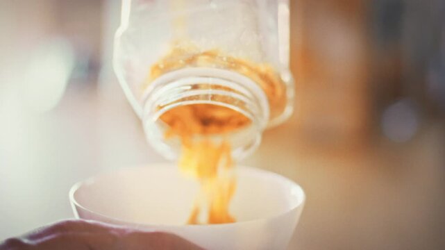 In cozy home kitchen, woman prepares nutritious breakfast by pouring cornflakes into a bowl. Her hands carefully handle the healthy food, reflecting her commitment to proper nutrition and a lifestyle