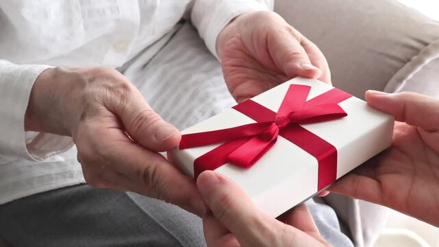 敬老の日／赤いリボンのプレゼントを受け取る高齢女性の手元