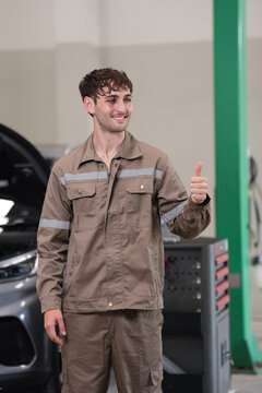 Mechanic car garage thumbs up uniform smiling man repair mechanic in garage giving thumbs up beside car, smiling with repair service confidence