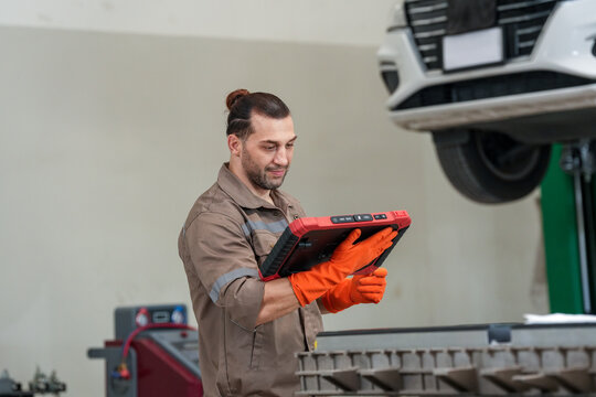 Car mechanic diagnostic tablet garage vehicle repair glove car mechanic using diagnostic tablet under raised vehicle in garage workshop