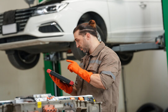 Mechanic car tablet glove garage repair service inspection focused worker uses digital tablet near lifted vehicle
