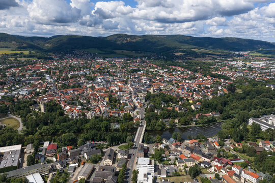 Aerial view of the historic town of Saalfeld with its dense urban layout, the Saale river, and surrounding green hills under a bright summer sky in Saalfeld, Thuringia, Germany.