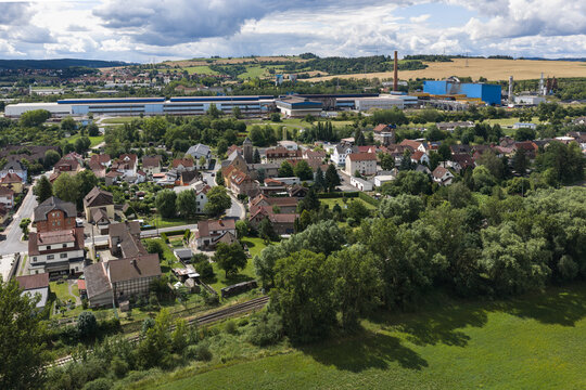 Aerial view of the town of Unterwellenborn featuring residential houses, lush greenery, and a large industrial factory complex in the background in Unterwellenborn, Thuringia, Germany.