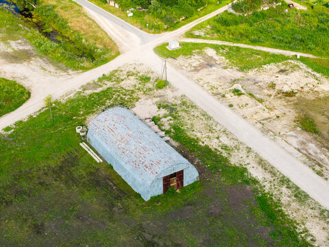 Aerial view of a metal Quonset hut situated in a rural field near dirt roads in Kalnciems, Jelgava Municipality, Latvia.