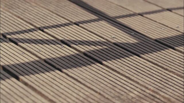 Soft shadows fall across a grooved wooden boardwalk creating an abstract geometric pattern in natural light.