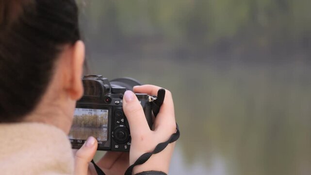 Person captures nature with camera. Focus on lake and trees. Calm moment near water. Good for travel or photography themes. Can use in advertising or educational content