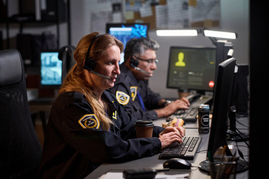 Caucasian woman security operator monitoring screens and typing at control desk, while male colleague assisting surveillance workflow. For cybersecurity or monitoring service marketing