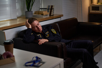 Obraz premium Caucasian security guard resting on office sofa during break, showing fatigue after shift. Image supporting workplace stress, burnout, staffing, employee wellness campaigns