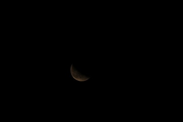 Deep space astrophotography of a detailed, earth-toned crescent moon against a pitch-black sky. © Valentin