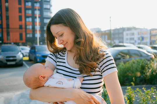Young mother sharing an tender moment with her sleeping newborn baby in an urban setting during golden hour, bonding through a loving connection and expressing happiness with parenthood