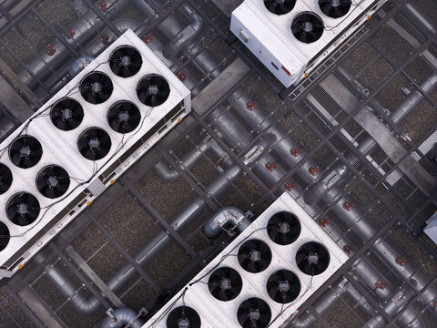 Aerial view of industrial HVAC cooling units with large fans and metal piping on a rooftop in Poland.