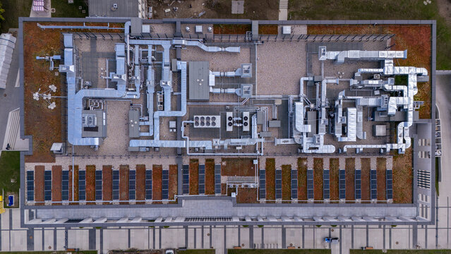 Aerial view of a flat building roof featuring complex metallic ventilation ducts, HVAC units, and rows of solar panels in Poland.