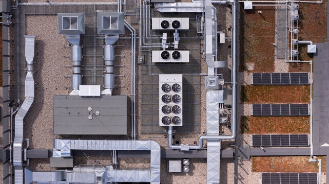 Aerial view of industrial rooftop featuring complex HVAC ventilation systems, metallic ductwork, and rows of solar panels in Poland.