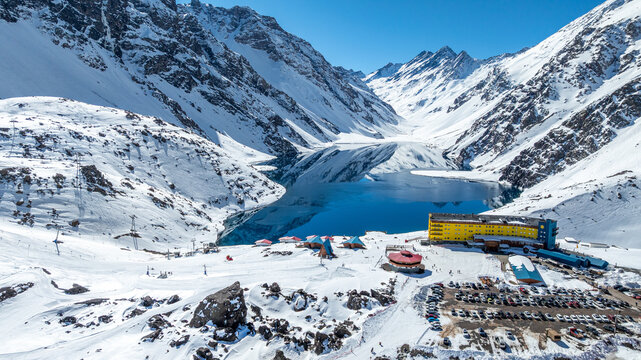 Aerial view of the Portillo ski resort, featuring the yellow hotel, a parking lot, and the Laguna del Inca surrounded by snow-covered Andes mountains in Portillo, Valparaiso, Chile.