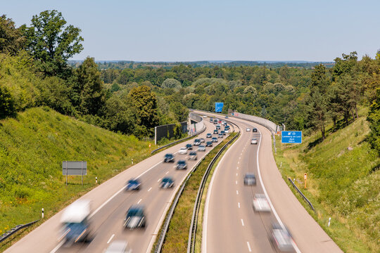 Traffic with blurred cars moving on german Autobahn A96 highway near Landsberg am Lech exit surrounded by green summer trees, high angle view