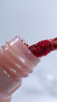 Red lipstick brush pulled from pink bottle in vertical front close up. Beauty cosmetic makeup applicator and packaging concept on clean white background.