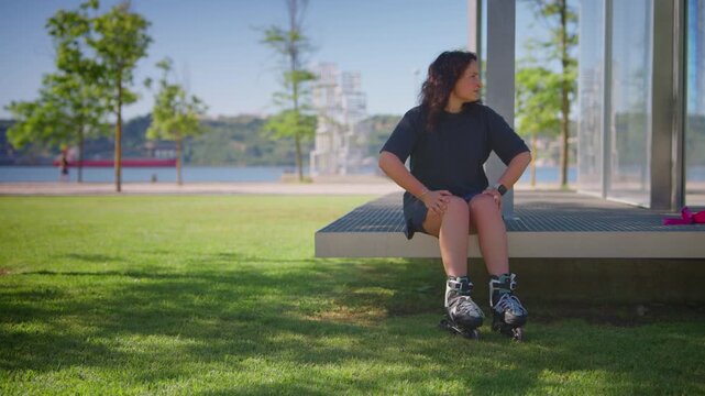 A casual roller skater enjoys a sunny day by the waterfront, preparing for an adventure while taking a break before gliding on the smooth pavement in the park.
