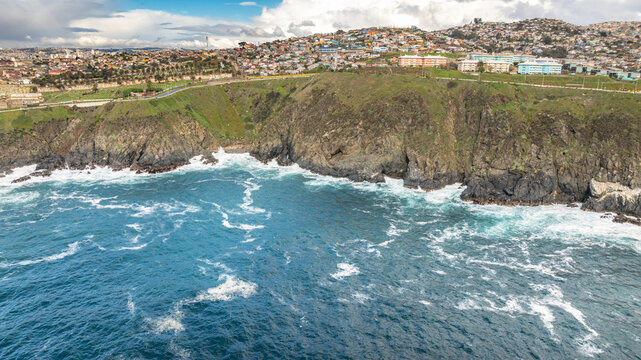 Aerial view of the rugged coastline and cliffs of Vina del Mar, with urban residential buildings perched on the hills overlooking the Pacific Ocean in Vina del Mar, Valparaiso, Chile.