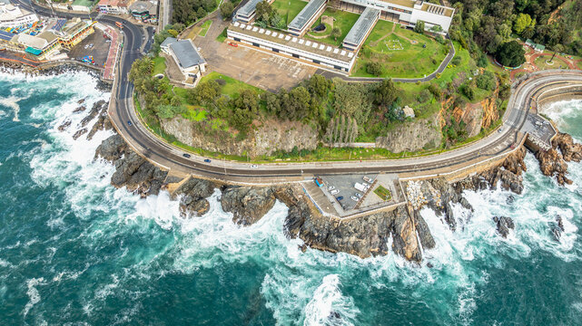 Aerial view of the coastal road winding along the rocky cliffs of the Pacific Ocean with modern buildings and green spaces in Vina del Mar, Valparaiso, Chile.
