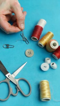 Clean studio style 4K flat lay showing craft scissors safety pins colored buttons and colorful thread spools arranged neatly on a solid blue background leaving generous copy space for DIY crafting
