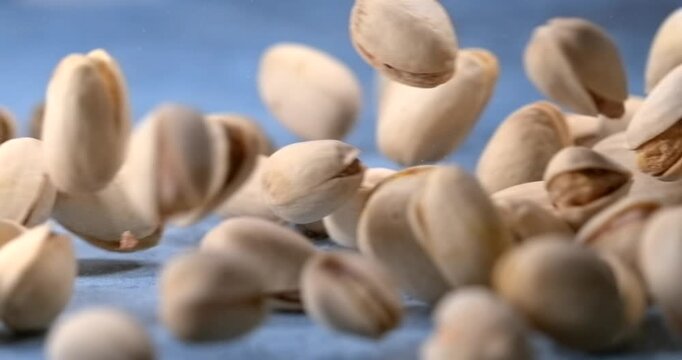 Pistachios fall and bounce across a blue table in slow motion