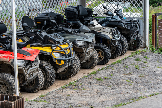 Row of colorful rental ATVs parked under a shelter outdoors on a summer day, ready for off road adventures and active recreation, with rugged tires and outdoor equipment in a leisure tourism setting