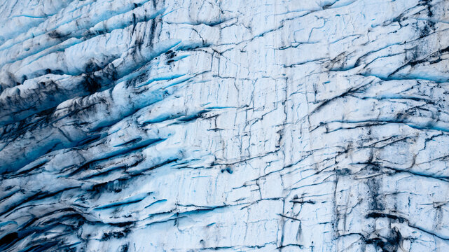 Aerial view of the textured surface of Valdez Glacier featuring deep blue crevasses, jagged ice formations, and intricate patterns in Valdez, Alaska, United States.