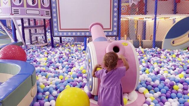 Little girl having fun in an indoor playground, playing in a colorful ball pit and shooting balls with an air cannon. Active childhood, family entertainment and recreation.