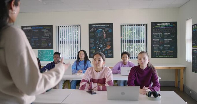 Diverse teenage students sitting in classroom with laptops raising hands answering teacher question