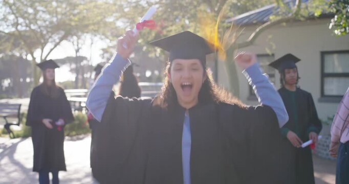 Diverse grads cheering as female grad in gown extending diploma, celebrating graduation together