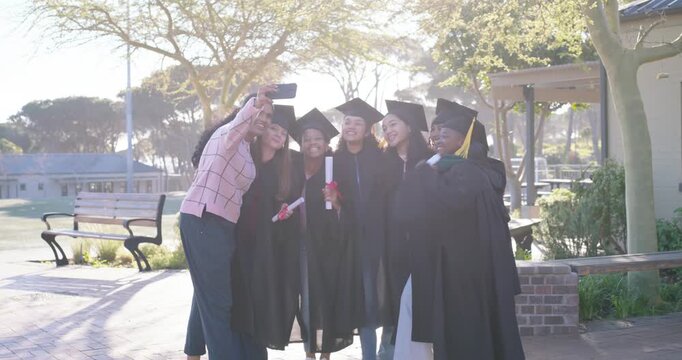 Diverse teenage grads posing in quad with diplomas, caps, gowns as organizer snapping smartphone