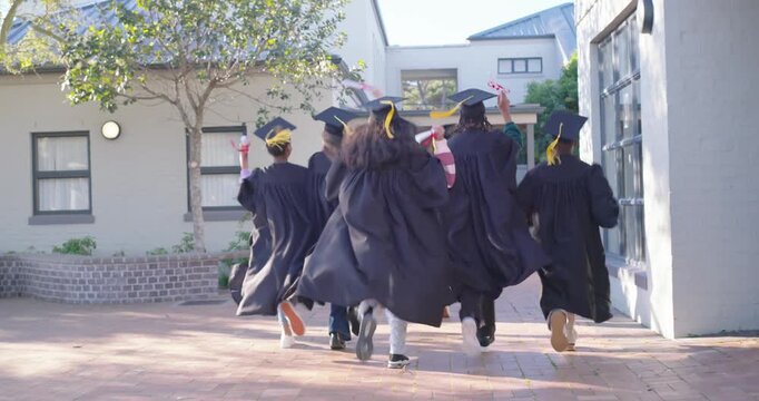 Diverse graduates moving down brick path in gowns and mortarboards, waving diplomas after ceremony