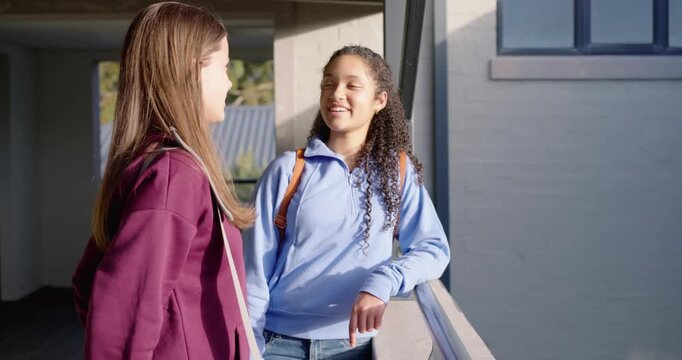 Teen females meeting after class on school balcony, in blue hoodie, leaning on railing, chatting
